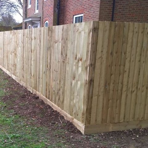 A white picket fence with gate and privet hedge, outside a cottage with a white door